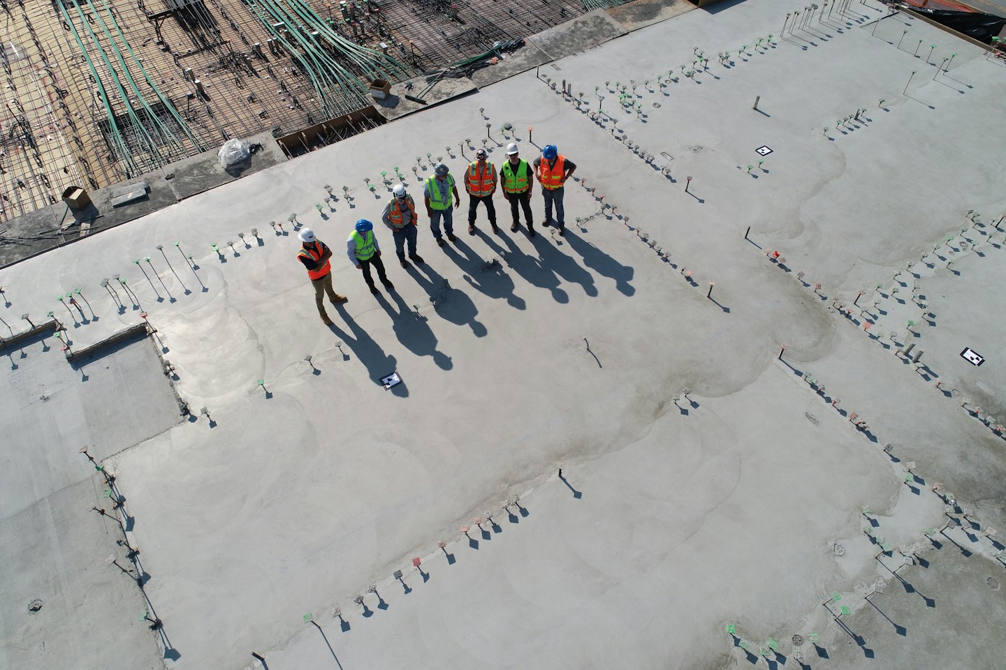 Construction workers in vests inspect an unfinished concrete site.
