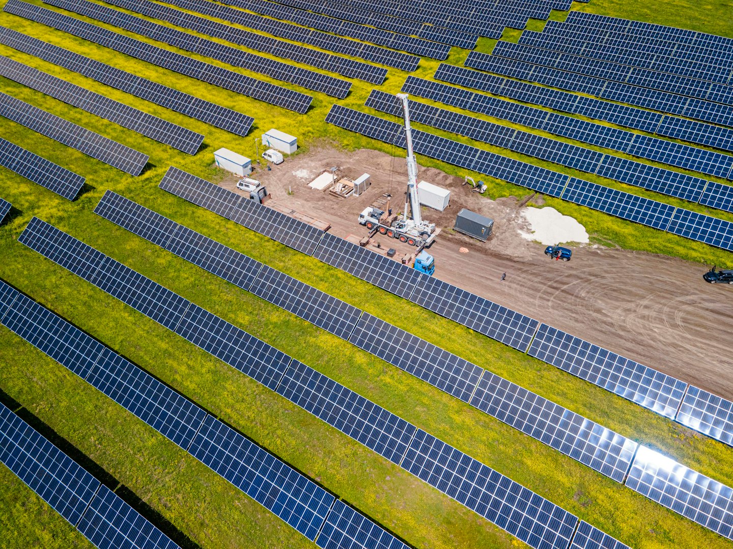 Solar panels stretch across green fields with a construction crane.