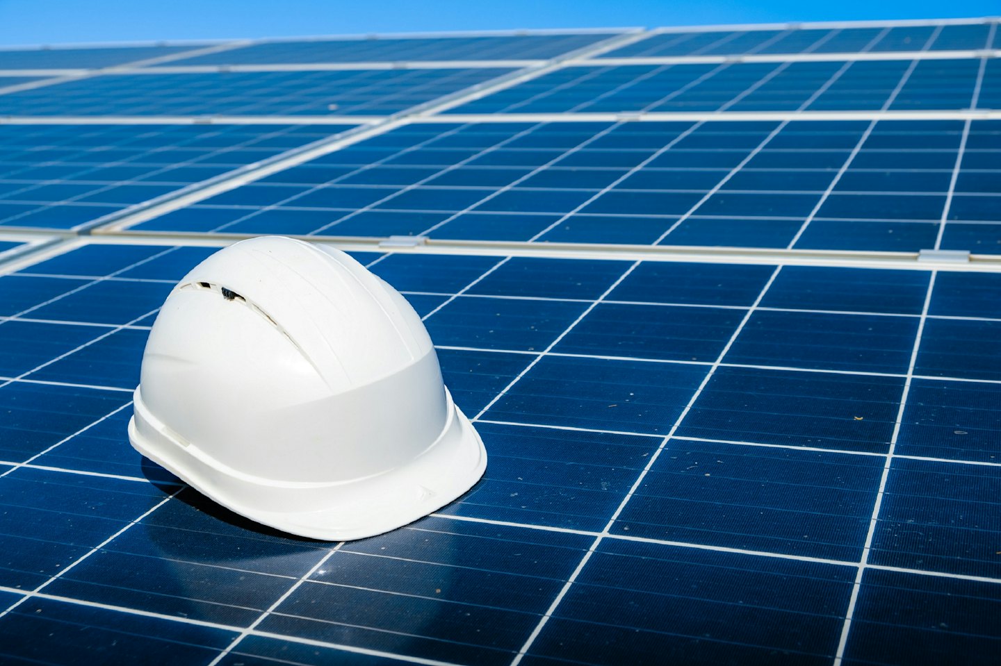 White hard hat resting on dark blue solar panels.